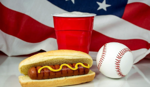 Hot dog surrounded by baseball game drink, flag and ball